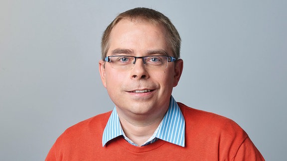 Ein Mann mit kurzen Haaren und Brille lächelt in die Kamera.