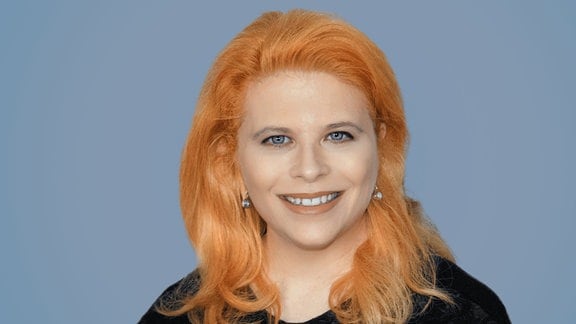 Eine Frau mit schulterlangen rötlichen Haaren lächelt in die Kamera.