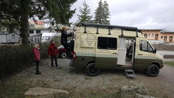 Drei Personen vor einem zum Campervan umgebauten Krankentransporter