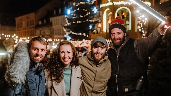 Eine Frau und drei Männer Arm in Arm auf einem Weihnachtsmarkt