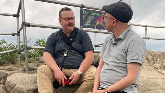 Zwei Männer sitzen auf einem Felsen und erzählen.