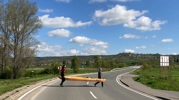 Zwei Personen tragen ein Boot über eine Straße.