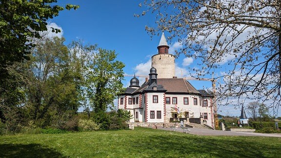 Ansicht einer Burg mit hohem mittleren Burgturm umgeben von Bäumen