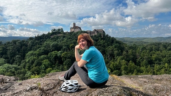 Frau sitzt auf einem Hügel vor der Wartburg