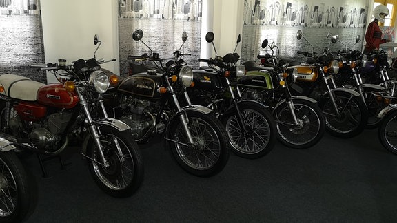 mehrere historische Motorräder aufgereiht in einem Museum
