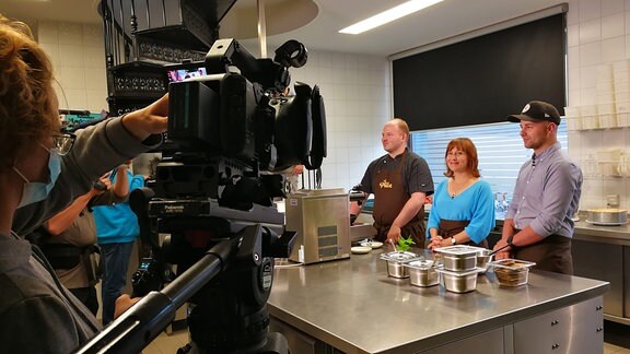 Ein Fernsehteam filmt drei Personen in einer Küche 