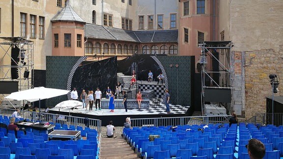 Ein Theaterstück auf einer Bühne vor einem Schloss. Vor der Bühne befindet sich eine große Zuschauertribüne 