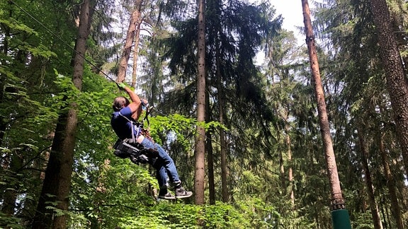 Ein Kameramann hängt an einem Seil im Kletterwald
