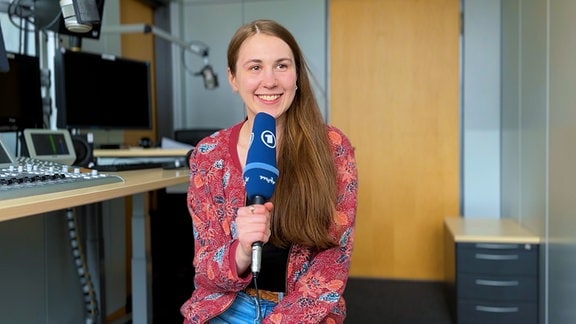 Volontärin Valerie Börner sitzt mit einem blauen MDR-Mikro in der Sprecherkabine.