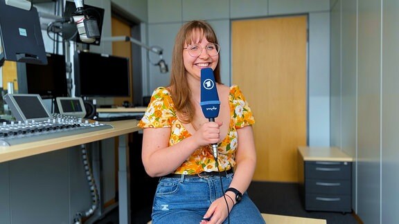 Volontärin Lonny Kirchner sitzt in einem Radiostudio und hält ein blaues MDR-Mikrofon in der Hand.