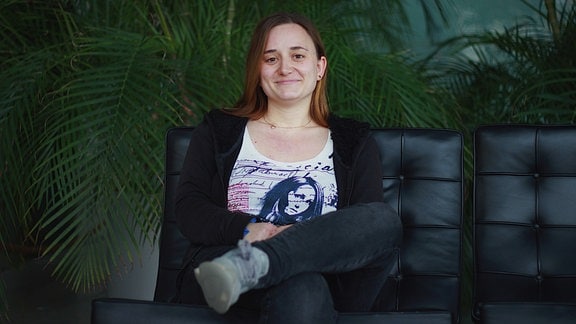 Volontärin Lea Hein auf einem schwarzen Lederstuhl vor einer Palme 