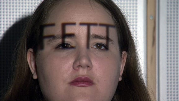 Eine Frau mit dem Schriftzug Fett auf dem Kopf