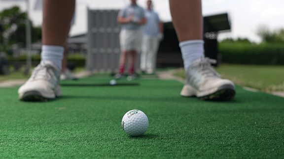 Frau auf Golfplatz. Nur die Beine sind zu sehen. Davor liegt ein Golfball.