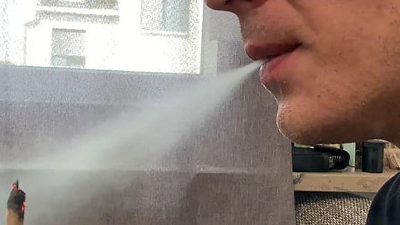 Ein Mann atmet Rauch aus, während er einen Joint hält.