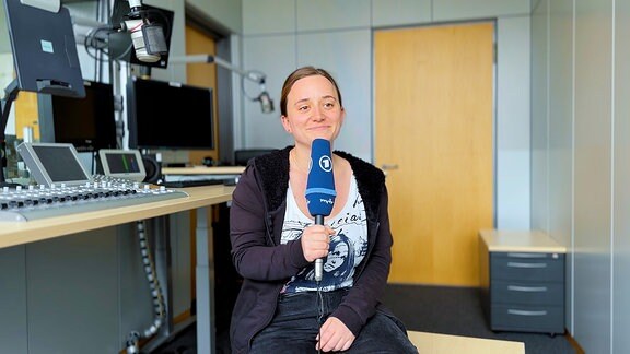 Volontärin Lea Hein sitzt in einem Radiostudio und hält ein blaues ARD-Mikrofon in der Hand