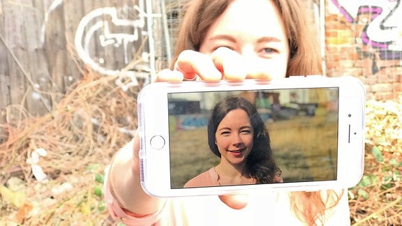 Eine junge Frau zeigt ein Smartphone mit einem Foto von sich
