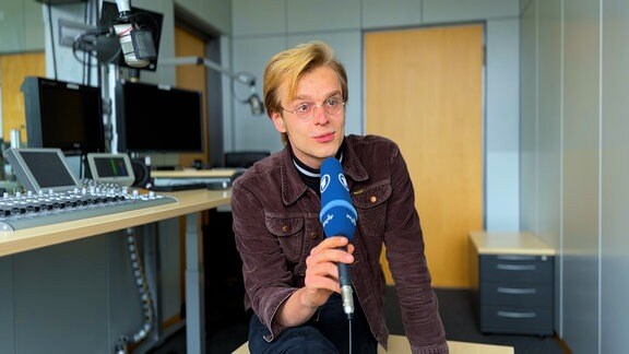 Volontär Lukas Stöckel sitzt mit einem Mikrofon in der Hand in einem Radiostudio.