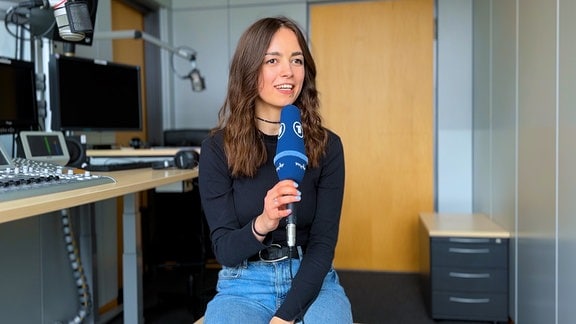 Volontärin Saskia Affolter sitzt mit einem blauen ARD-Mikrofon in der Hand in einem Radiostudio.