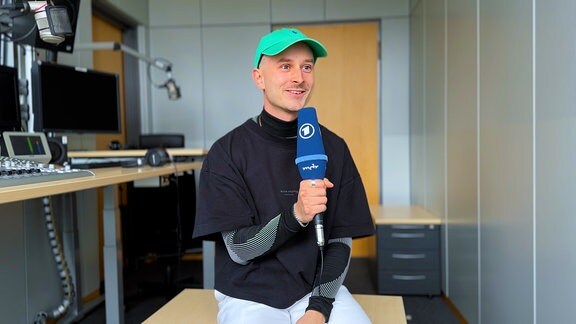 Volontär Til Schäbitz sitzt mit einem ARD-Mikrofon in der Hand in einem Radio-Studio