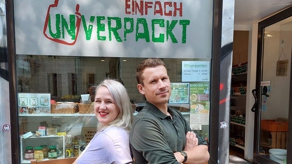 Eine junge Frau und ein junger Mann Rücken an Rücken vor einem Laden