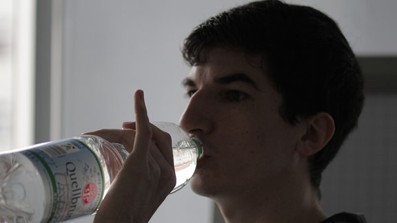 Ein junger Mann trinkt aus einer Wasserflasche und hat dabei den kleinen Finger abgespreizt.