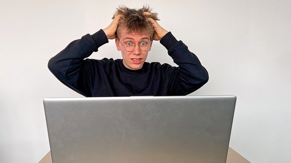 Ein junger Mann sitzt verzweifelt vor einem Laptop und rauft sich die Haare.