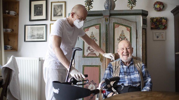  Altenpfleger mit Corona-Maske bei der Arbeit mit Patient in haeuslichen Umfeld Heidelberg 