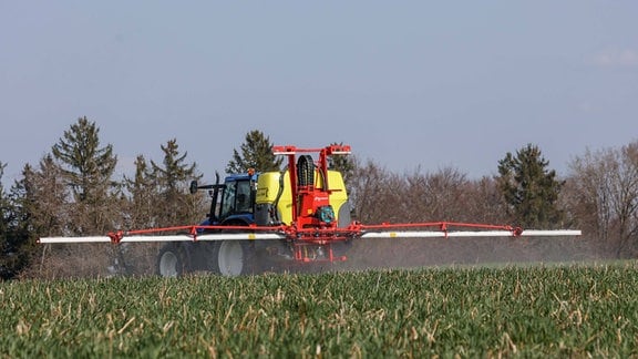 Ein Landwirt fährt mit seinem Traktor mit Pflanzenschutzspritze über ein Feld