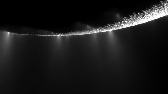 Aufnahme der Raumsonde Cassini, die den Saturnmond Enceladus überpfliegt. Dort steigen Fontänen aus Wassereis über der Mondoberfläche auf