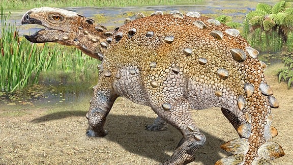 3D-Modell: Dinosaurier mit spitzer, gebogener, offener Schnauze, zackigem Rückenpanzer und Schwanz mit breitem Ende steht in Flusslandschaft. Im Hintergrund Hügel.