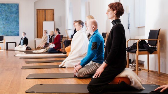 Mehrere Personen knien meditierend auf Matten.