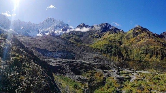 Panorama-Aufnahme von Berggipfeln und grünen Hängen im Hochland von Tibet. 