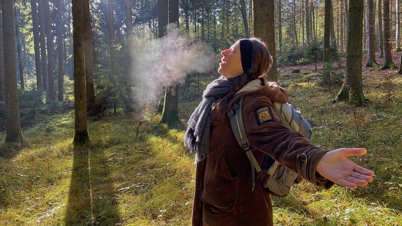 Eine Frau atmet in einem Wald aus.
