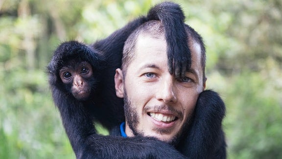 Ein Mann hält einen kleinen schwarzen Affen