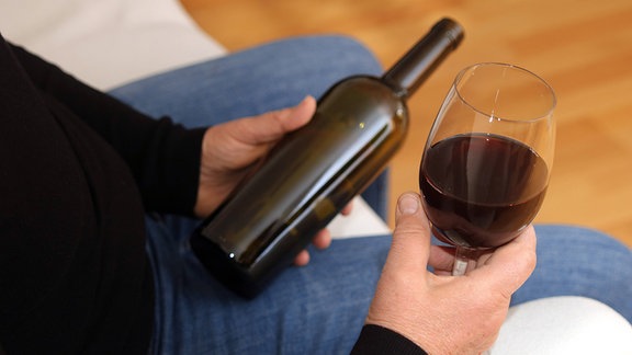 Ein Mann mit einer Rotweinflasche und Rotweinglas.