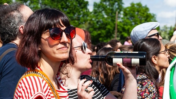 Eine junge Frau in einer Zuschauermenge trinkt aus einer Weinflasche.