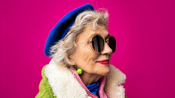 Modische Seniorin mit blauer Mütze und Sonnenbrille.