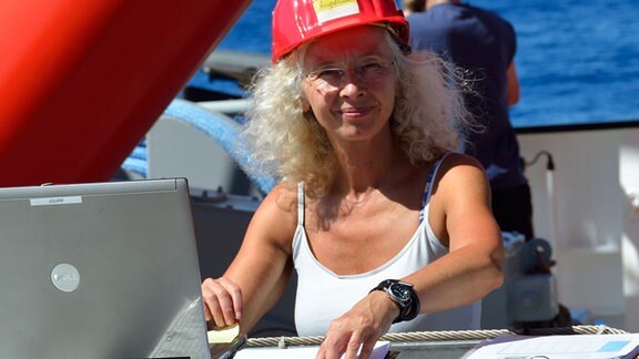 eine Frau mit rotem Basecap vor einem Laptop auf einem Schiff