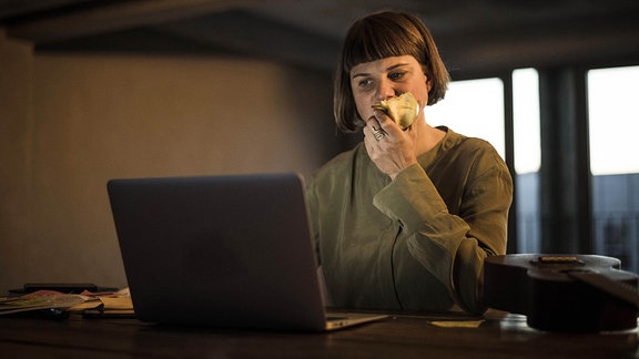 Eine Frau vor einem Laptop beißt in einen Apfel.