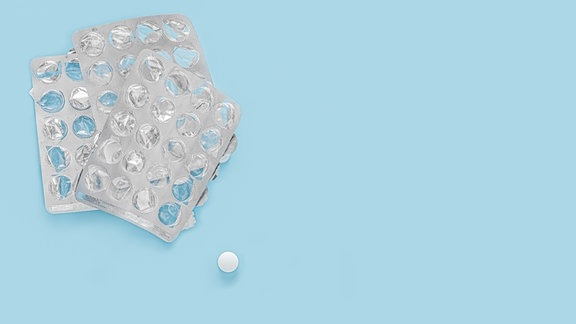 Drei typische silberne Tablettenpackungen, aus denen alle Tabletten bereits entnommen wurden. Daneben eine einzelne weiße Tablette.
