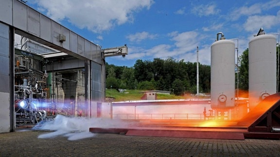 Ein Heißfeuer-Test eines Raketentriebwerkes am DLR-Standort in Lampoldshausen. Rechts befindet sich das Triebwerk in seiner Wagerechten und feuert zur linken Bildhälfte hin.