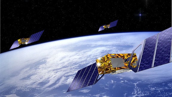 Eine künstlerische Darstellung des Galileosatelliten der europäischen Raumfahrtbehörde ESA. In der unteren Bildhälfte befindet sich die Erde, in der oberen Hälfte das Weltall. Drei Satelliten umkreisen die Erde, einer links und einer rechts im Hintergrund. Der dritte Satellit befindet sich im rechten Vordergrund und ist an der Seite vom Billdrand abgeschnitten.