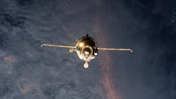 Das russische Sojus-Raumschiff auf dem Weg zurück zur Erde. Im Hintergrund sieht man eine Wolkendecke.