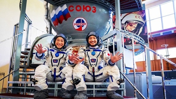 Die japanischen Weltraumtouristen Yusaku Maezawa und Yozo Hirano in ihren russischen Raumanzügen vor einem Sojus-Raumschiff.