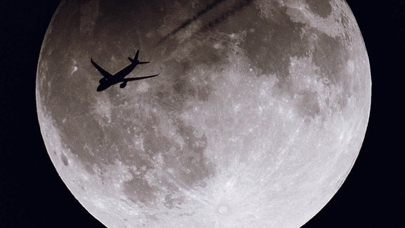 Silhouette eines Flugzeugs vor dem Mond