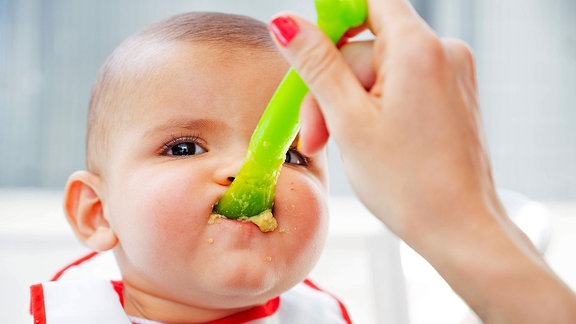 Ein Baby wird mit einem grünen Löffel gefüttert
