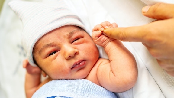 Neugeborenes im Krankenhaus, nach dem Finger seiner Mutter greifend