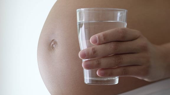 Eine Frau mit Babybauch hält ein Glas Wasser