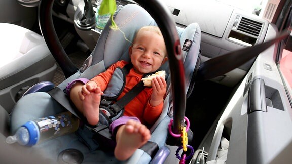 Kleines Kind liegt angeschnallt in Babyschale im Auto.