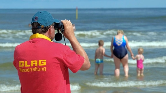 Mitglied der DLRG Wasserrettung steht am Strand der Insel Spiekeroog und beobachtet Schwimmer in den Wellen der Nordsee.